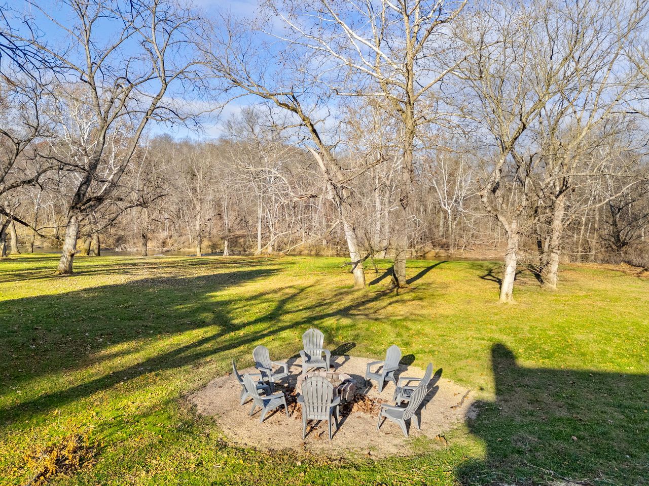 A circular outdoor seating area with chairs and a fire pit surrounded by grass and trees.