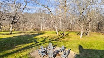 A circular outdoor seating area with chairs and a fire pit surrounded by grass and trees.