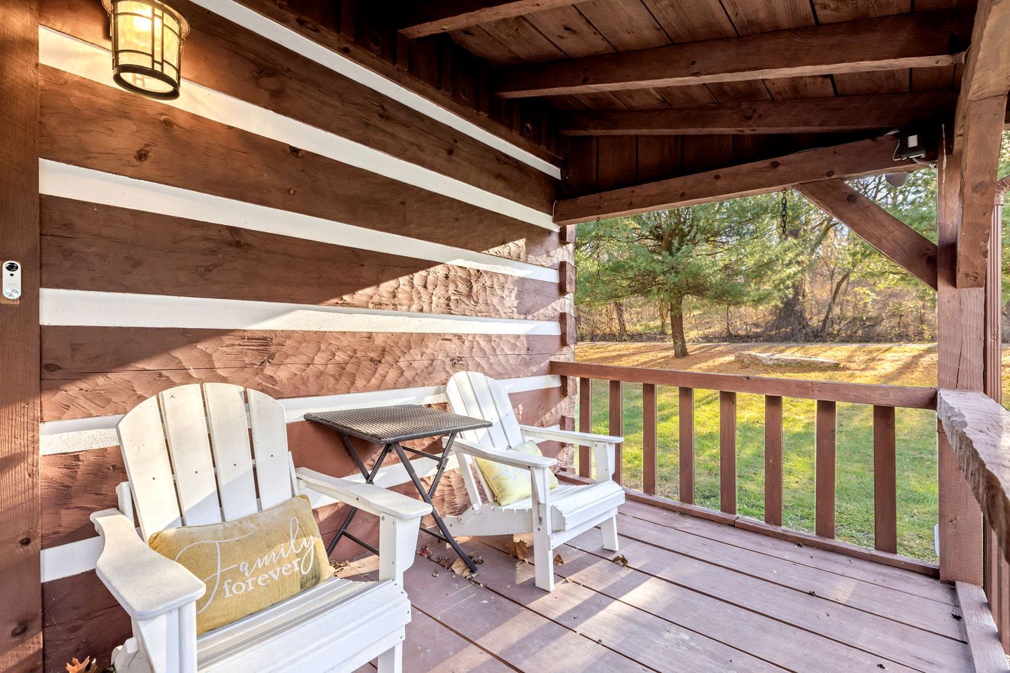 A wooden deck with Adirondack chairs and a table, overlooking a grassy area with trees.