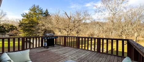 A deck with a grill, seating area, and a view of a grassy field with trees.