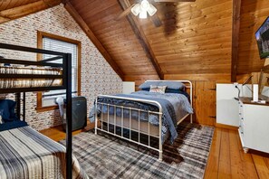 A cozy attic bedroom with a bunk bed, a single bed, and a wooden ceiling.