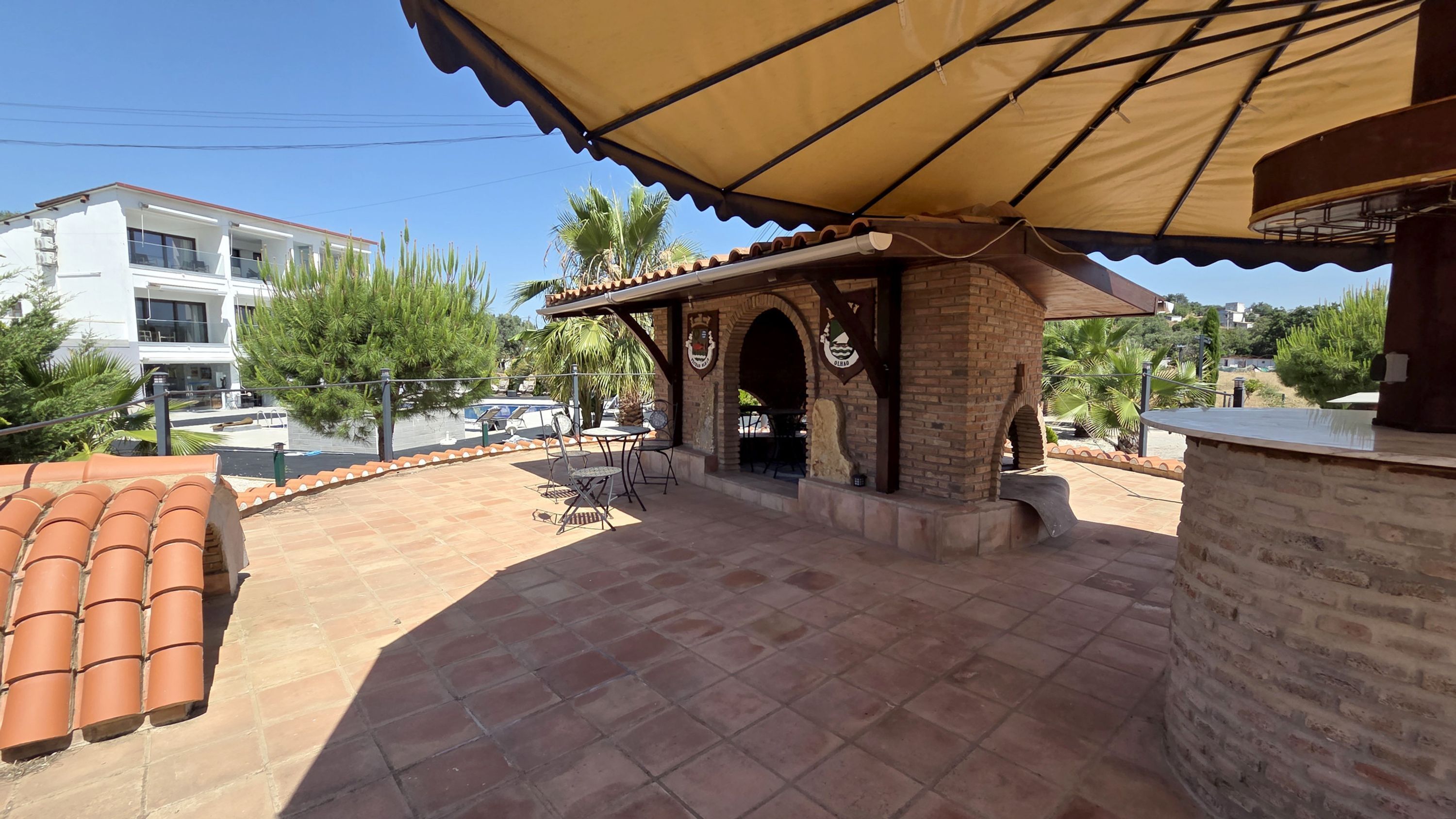A patio area with a brick wall, a covered seating area, and a view of a residential building in the background.