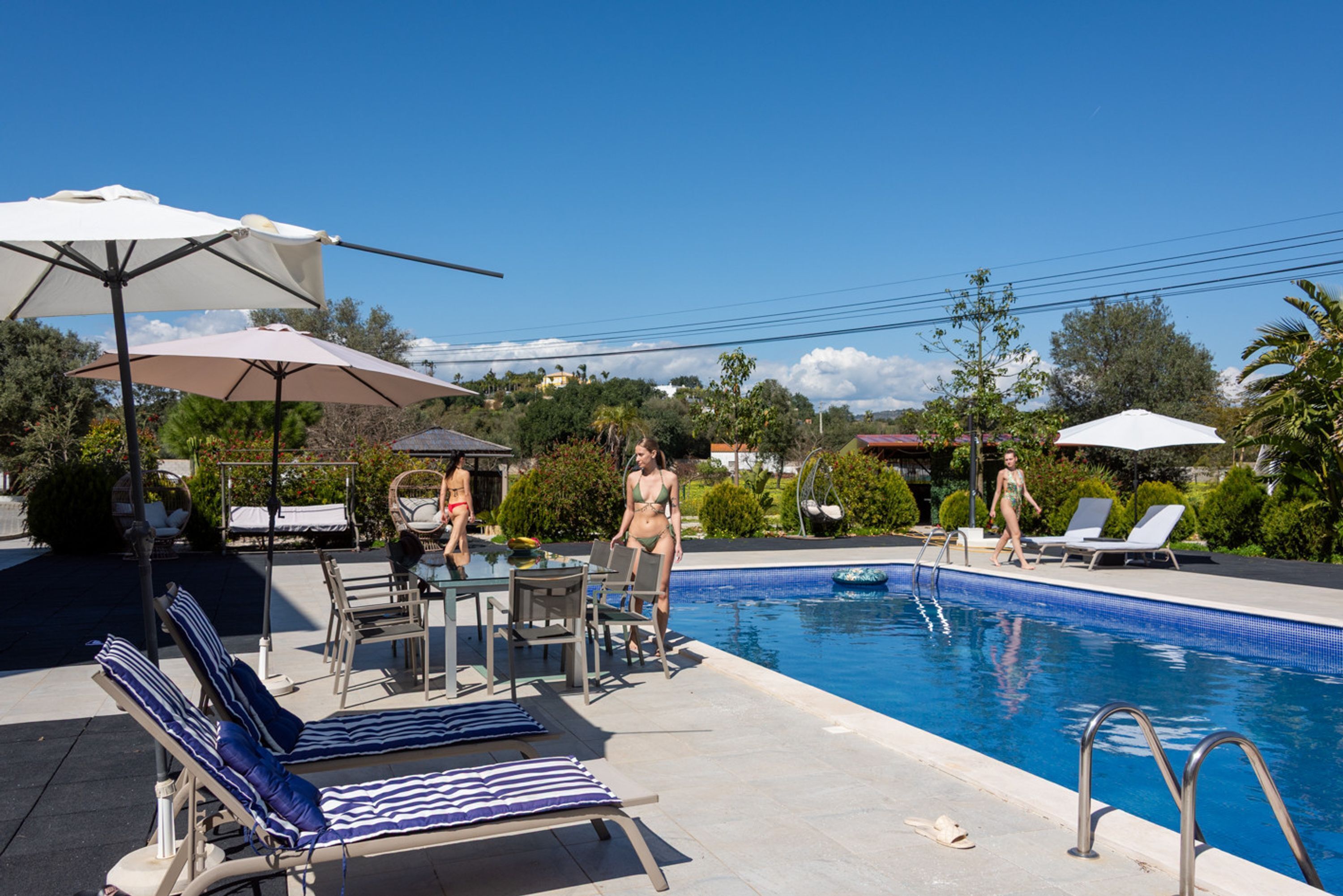 A poolside area with lounge chairs, umbrellas, and a clear blue sky.