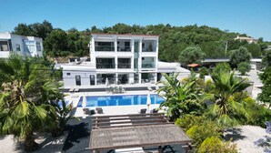 A modern two-story building with a swimming pool, surrounded by palm trees and a covered outdoor seating area. - Vale Paraiso Relax Lounge (Olhao)