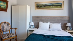 A hotel room with a bed, a nightstand, a chair, a wardrobe, and a landscape painting on the wall. - Vale Paraiso Relax Lounge (Olhao)