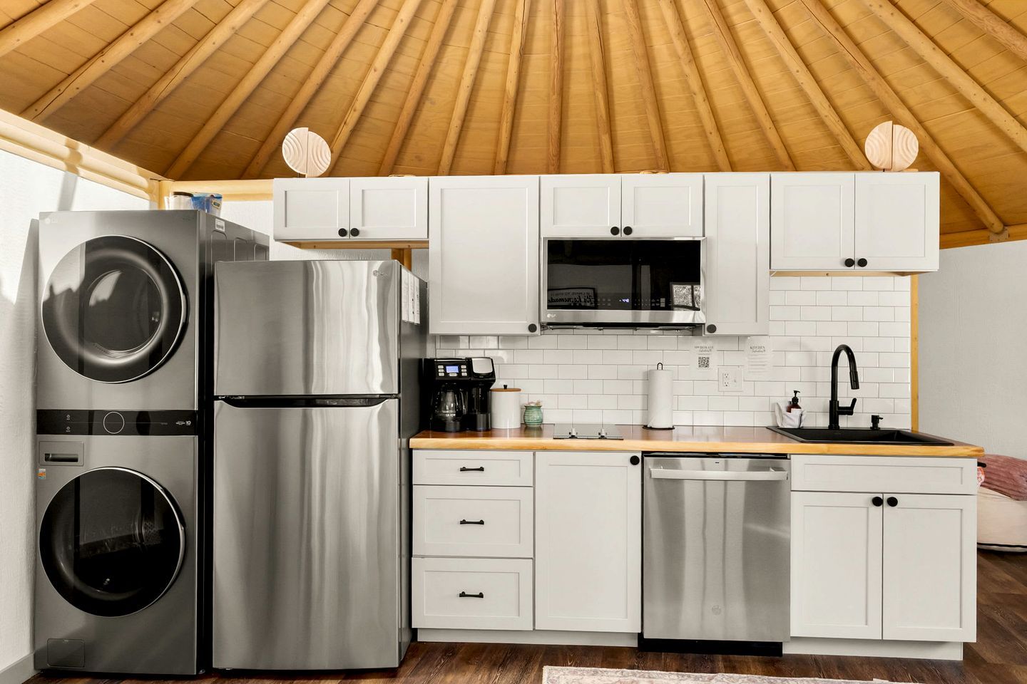 A compact kitchen with stainless steel appliances, white cabinetry, and a wooden ceiling.