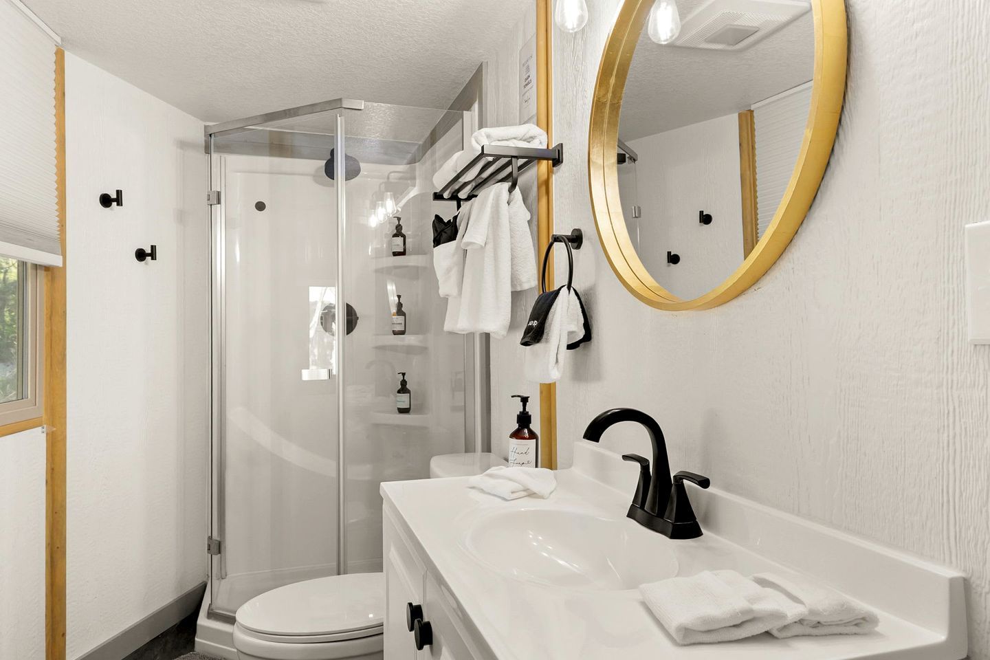 A modern bathroom with a glass shower enclosure, a white sink with a black faucet, and a large mirror with a gold frame.