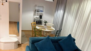 A modern living room with a teal sofa, a dining table with chairs, a white cabinet, and a large window with curtains. - "Between Sky and Sea" Apartment in Pescara. Sea: 200 m. University 700 m.  Parking (Pescara)