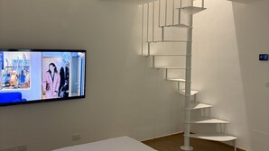 A hotel room with a bed, a TV mounted on the wall, and a spiral staircase. - "Between Sky and Sea" Apartment in Pescara. Sea: 200 m. University 700 m.  Parking (Pescara)