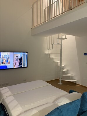 Ein Hotelzimmer mit einem Bett, einem an der Wand befestigten Fernseher und einer Wendeltreppe.