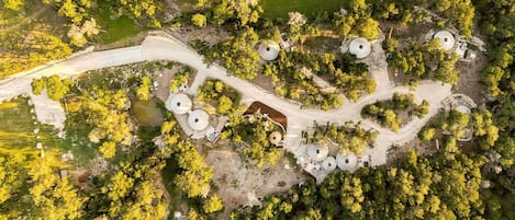 An aerial view of a property with a winding road, several round structures, and dense greenery.