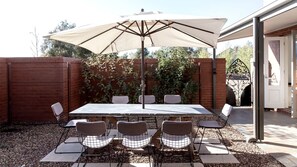 A patio with a table and chairs, an umbrella, and a brick wall with climbing plants. - Luminous Elegant Rental with Patio and Landscape Views in Victoria (Daylesford)