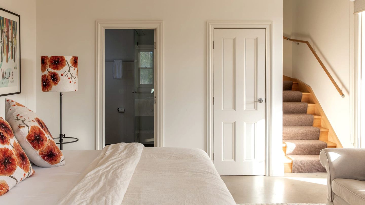 A bedroom with a bed, a nightstand, a lamp, a door, and a staircase.