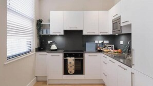 A modern kitchen with white cabinets, a black countertop, a kettle, and a microwave. - Stylish One-Bed Apartment in the Heart of Historic Bath (Bath)