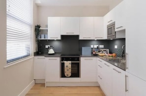 A modern kitchen with white cabinets, a black countertop, a kettle, and a microwave. - Stylish One-Bed Apartment in the Heart of Historic Bath (Bath)