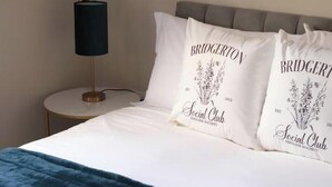 A bed with two pillows featuring the Bridgerton logo and a lamp on a bedside table. - Stylish One-Bed Apartment in the Heart of Historic Bath (Bath)