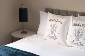 A bed with two pillows featuring the Bridgerton logo and a lamp on a bedside table. - Stylish One-Bed Apartment in the Heart of Historic Bath (Bath)