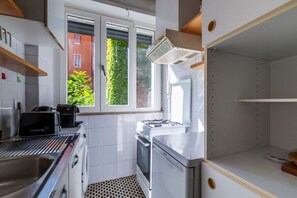 Eine Küche mit weißen Schränken, einem Gasherd, einem Toaster und einem Fenster mit Blick ins Grüne.