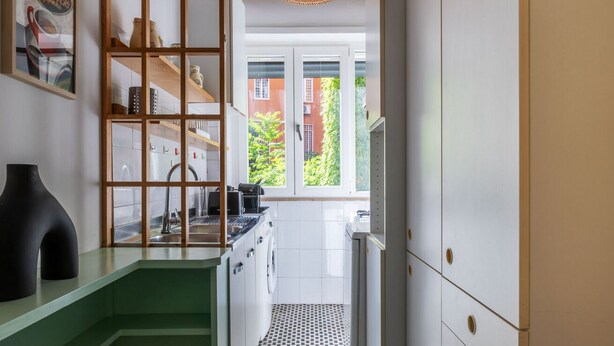Een moderne keuken met een groen aanrecht, een hanglamp en uitzicht op een gebouw van rode baksteen door het raam.