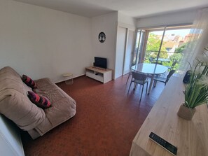 A living room with a sofa, a TV stand, a dining table with chairs, and a view of the outside. - Apartment with AC, sea view - 3 guests (Collioure)