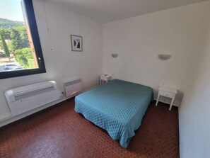 A bedroom with a bed, a nightstand, a window, and a radiator. - Apartment with AC, sea view - 3 guests (Collioure)