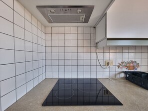 A kitchen with white tiled walls, a black induction cooktop, and a stainless steel range hood. - Apartment with AC, sea view - 3 guests (Collioure)