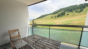 En balkon med træbænk og stol, der udover et grønt landskab med træer og en bakke.