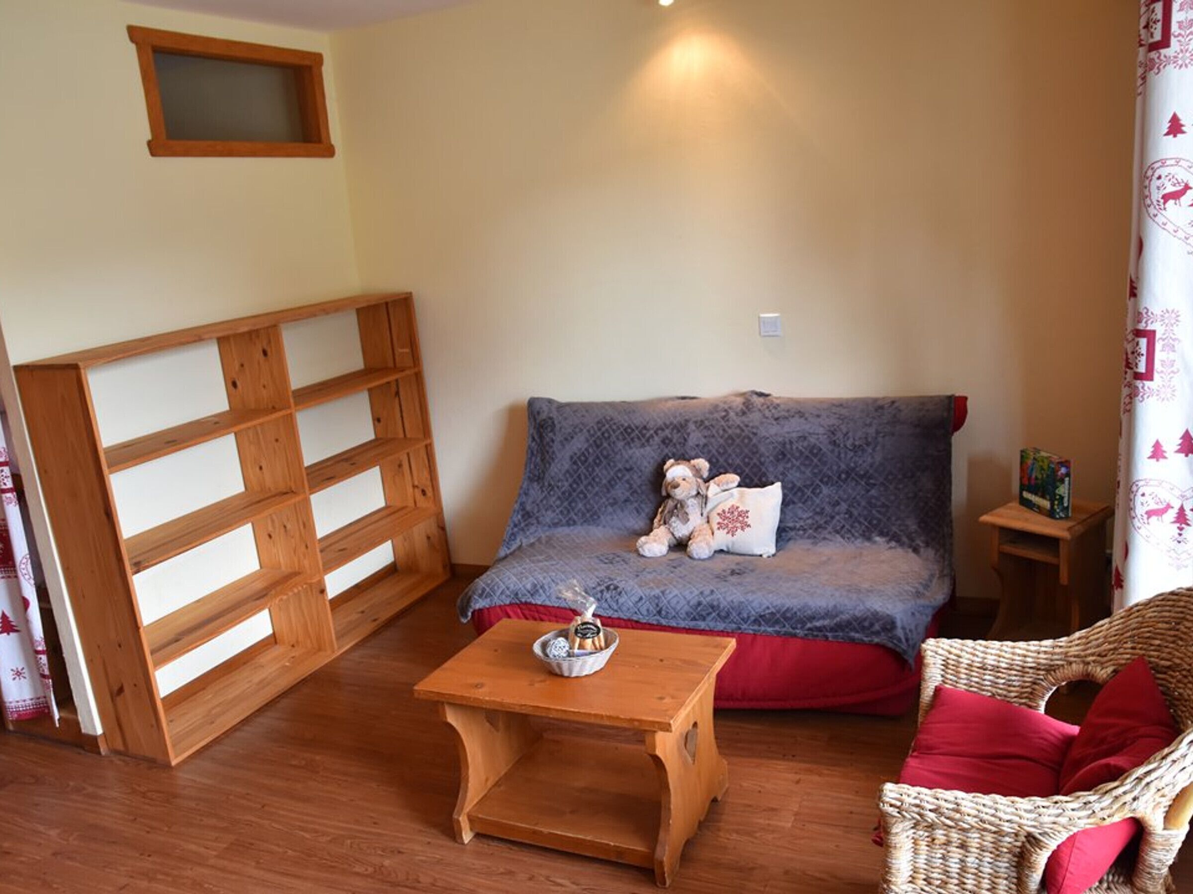 A cozy room with a wooden bench, a small table with a candle, a sofa with a teddy bear, and a wicker chair.