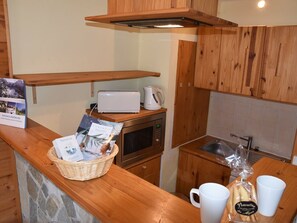 A kitchen with wooden cabinets, a microwave, a toaster, and a basket of welcome items. - Studio near slopes - 4 guests (Montgenèvre)