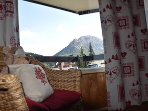 A cozy room with a wicker sofa, a red cushion, and a view of a mountain. - Studio near slopes - 4 guests (Montgenèvre)