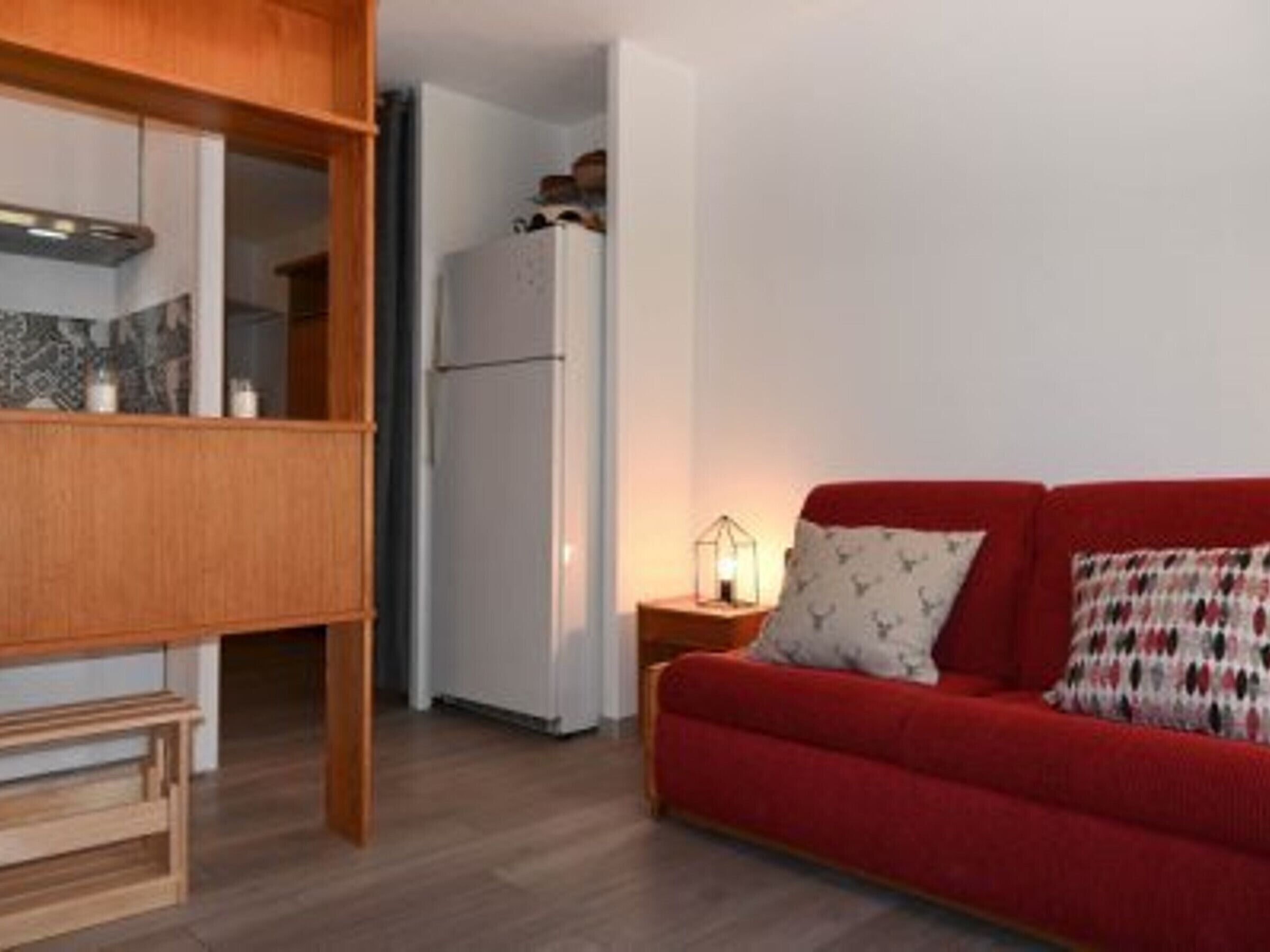 A compact living space with a red sofa, wooden cabinet, and a white refrigerator.