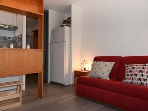 Ein gemütlicher Wohnbereich mit einem roten Sofa, einem Holzkasten und einem weißen Kühlschrank.