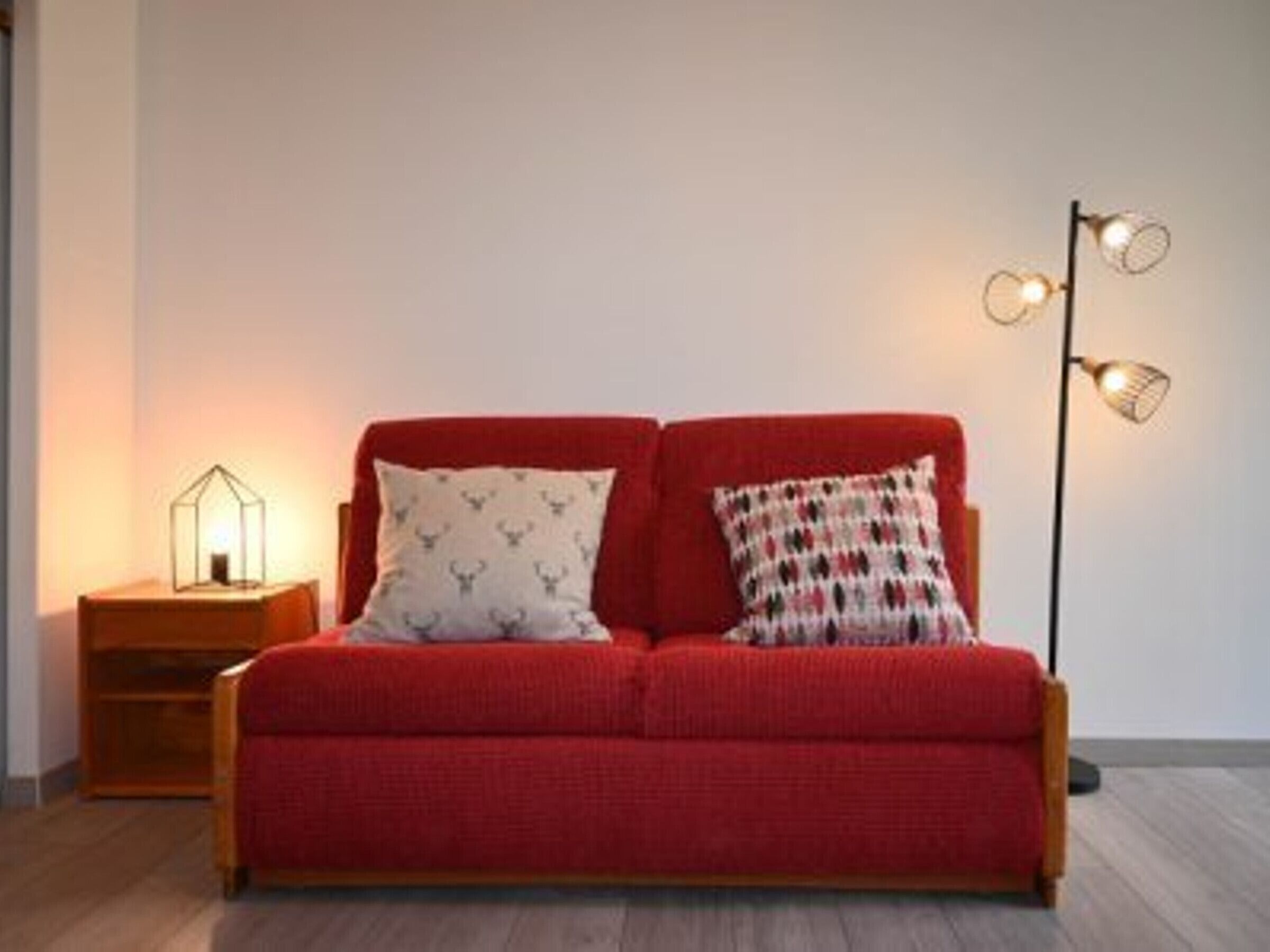 Un canapé rouge avec deux coussins, une lampe sur pied et une petite table avec une lampe.
