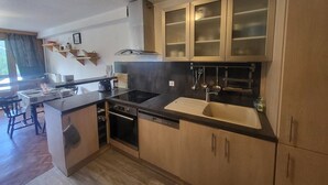 A compact kitchen with a dishwasher, stove, and sink. There is a dining area with a table and chairs. - Sunny studio with south balcony - 2 guests (Montgenèvre)