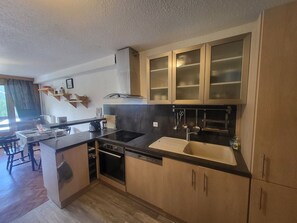 Cozinha compacta com lava-louças, fogão e pia. Há uma área de jantar com mesa e cadeiras.
