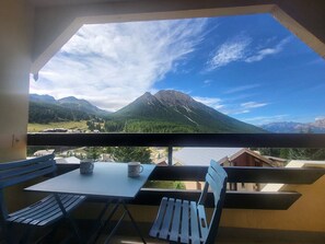Varanda com mesa e cadeiras, vista para uma paisagem montanhosa sob um céu claro.