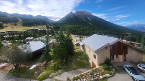 A mountain lodge with a view of a mountain range, surrounded by greenery and a few buildings. - Sunny studio with south balcony - 2 guests (Montgenèvre)