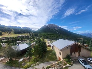Uma hospedaria nas montanhas com vista para uma cordilheira, rodeada por vegetação e alguns edifícios.