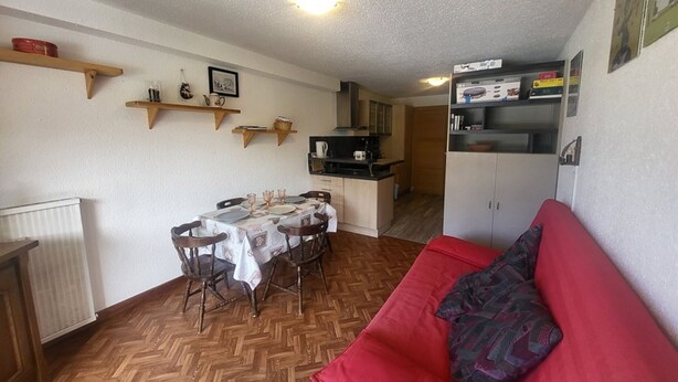 A compact living space with a dining table set for four, a red sofa, and a kitchenette area. - Sunny studio with south balcony - 2 guests (Montgenèvre)