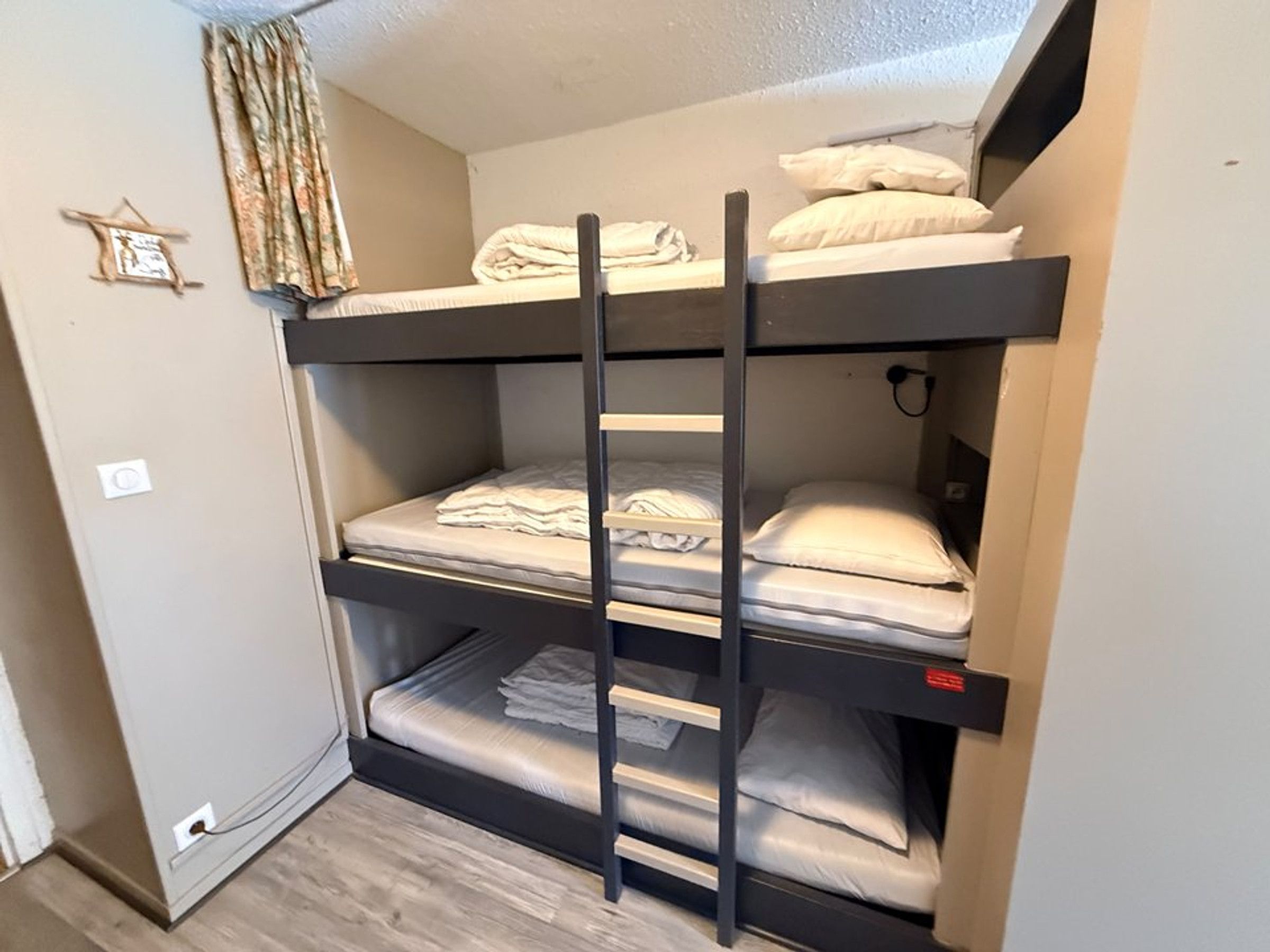 Un lit superposé à trois niveaux, une prise de courant et un petit objet décoratif accroché au mur.