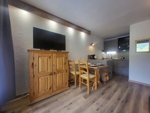 A compact kitchen with wooden cabinets, a dining table with chairs, and a flat-screen TV mounted above the cabinets. - Studio with wifi - Piste view, 2 guests (Montgenèvre)