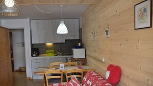 A cozy living room with a wooden floor, a red patterned sofa, and a dining area with a wooden table and chairs. - Studio with pets allowed, parking - 4 guests (Montgenèvre)