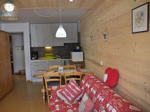 A cozy living room with a wooden floor, a red patterned sofa, and a dining area with a wooden table and chairs. - Studio with pets allowed, parking - 4 guests (Montgenèvre)