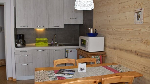 A compact kitchen with grey cabinets, a microwave, and a sink. There's a wooden dining table with chairs and a hanging light fixture. - Studio with pets allowed, parking - 4 guests (Montgenèvre)