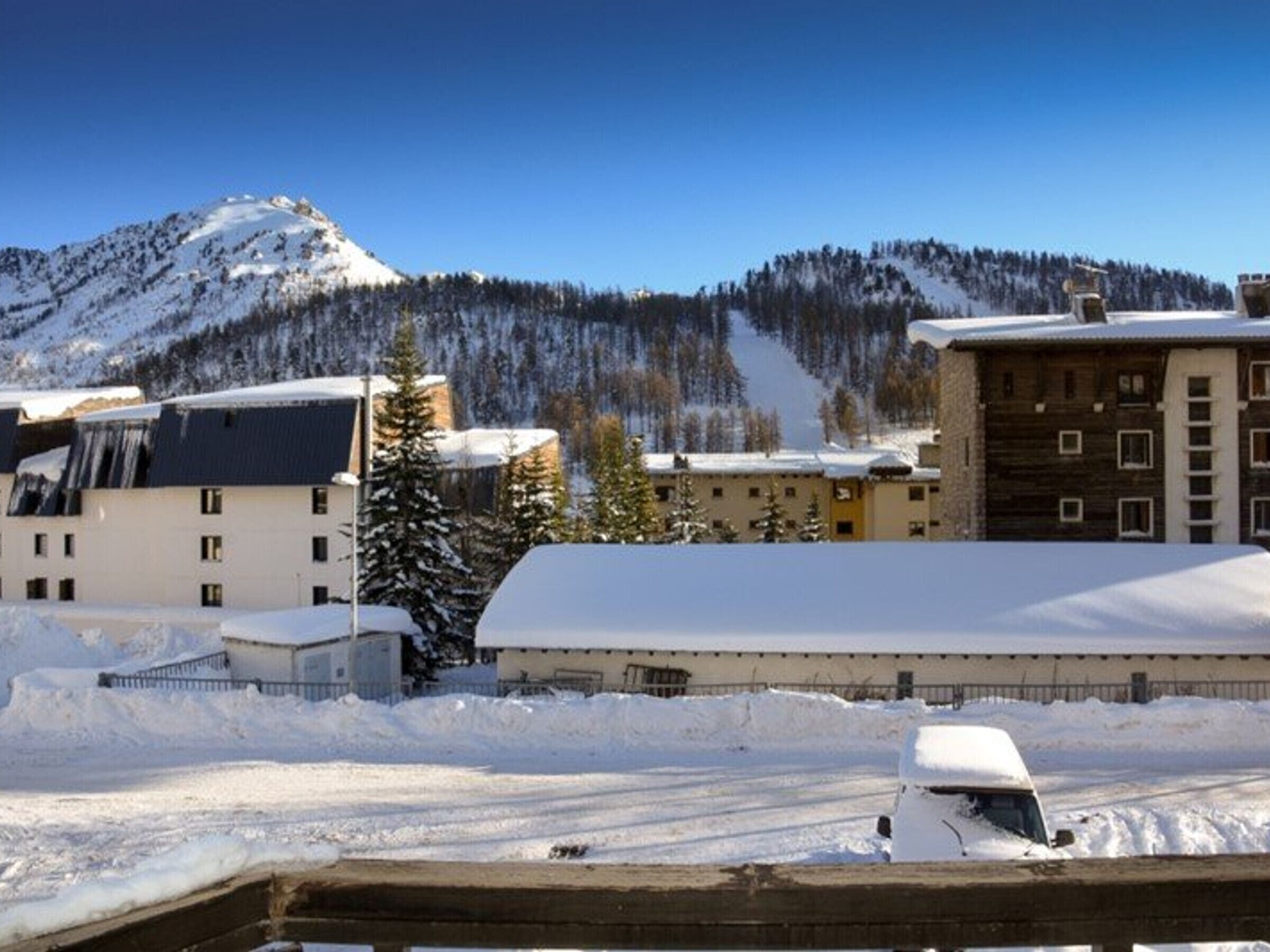 A hotel with a snow-covered roof, a mountain in the background, and a clear sky.