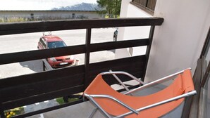 A balcony with a metal-framed orange chair, a green chair, and a red car parked in the background. - Studio with pets allowed, parking - 4 guests (Montgenèvre)