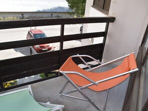 A balcony with a metal-framed orange chair, a green chair, and a red car parked in the background. - Studio with pets allowed, parking - 4 guests (Montgenèvre)