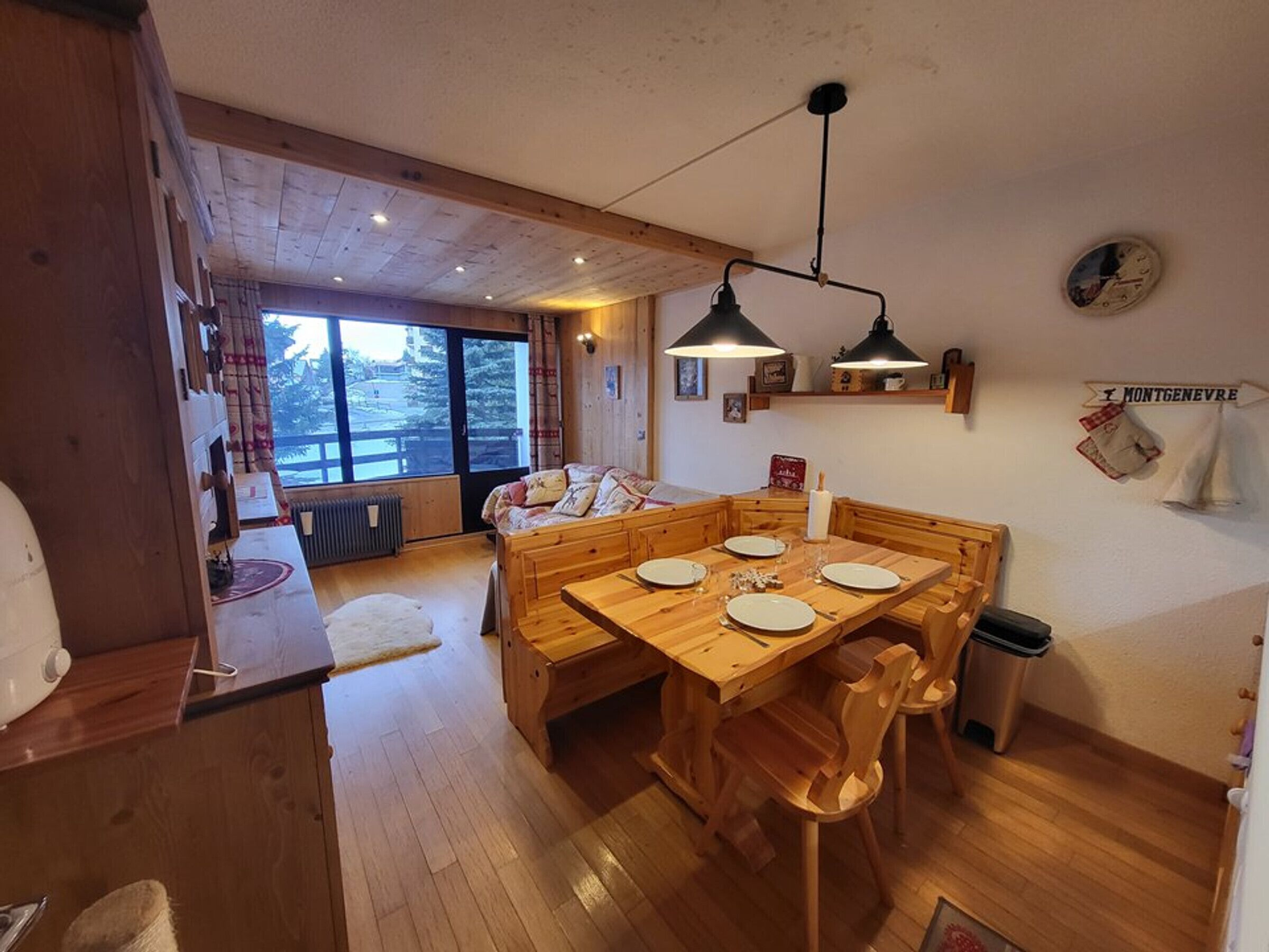 Una mesa de madera para comer con sillas, un banco de madera, una ventana con vistas y un cartel en la pared.