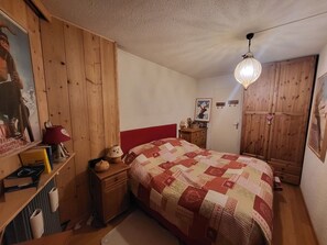 Ein Schlafzimmer mit einem Holfischschrank, einem Bett mit Steppdecke, einem Nachttisch, einer Lampe und einem Poster an der Wand.