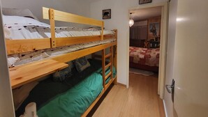 Ein Zimmer mit Etagenbetten, einem Holztisch und einer Tür zu einem anderen Raum.